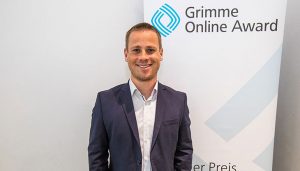 Chefredakteur Yannick Dillinger bei der Bekanntgabe der Nominierung in Köln, vor einem Rollup des Grimme Online Award; Foto: Rainer Keuenhof/Grimme-Institut